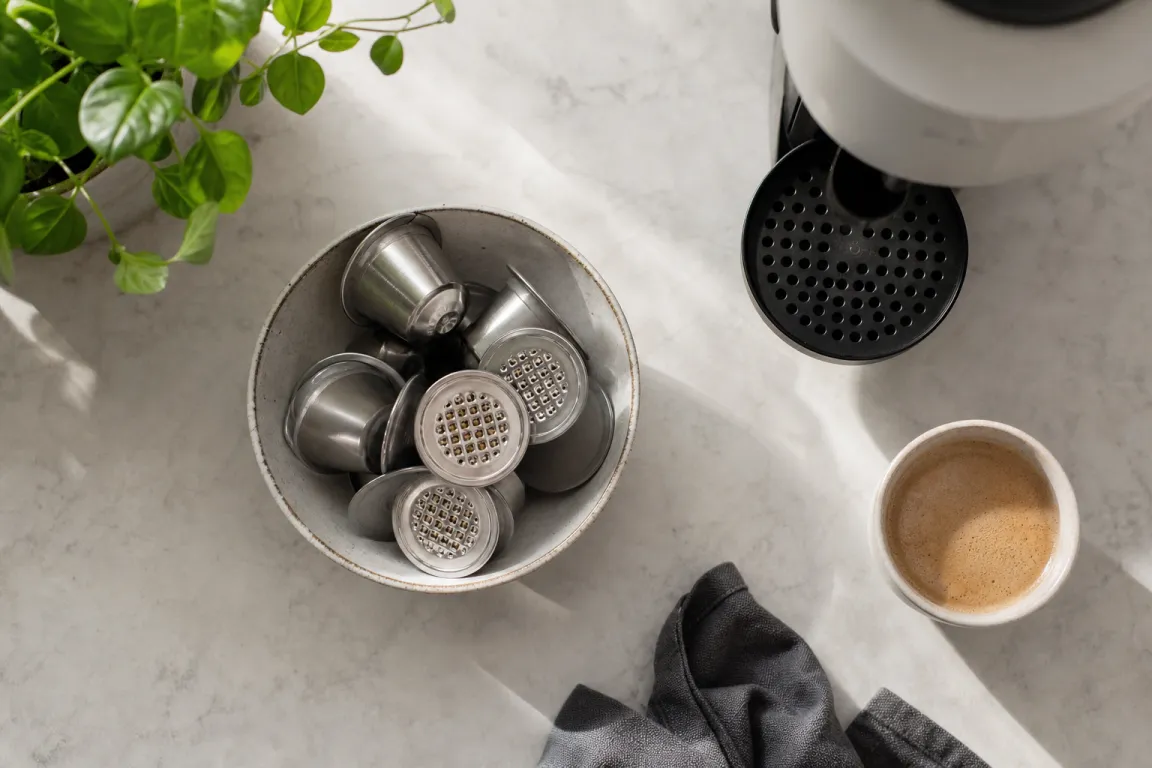 Återanvändbar kaffekapsel i metall bredvid malet kaffe