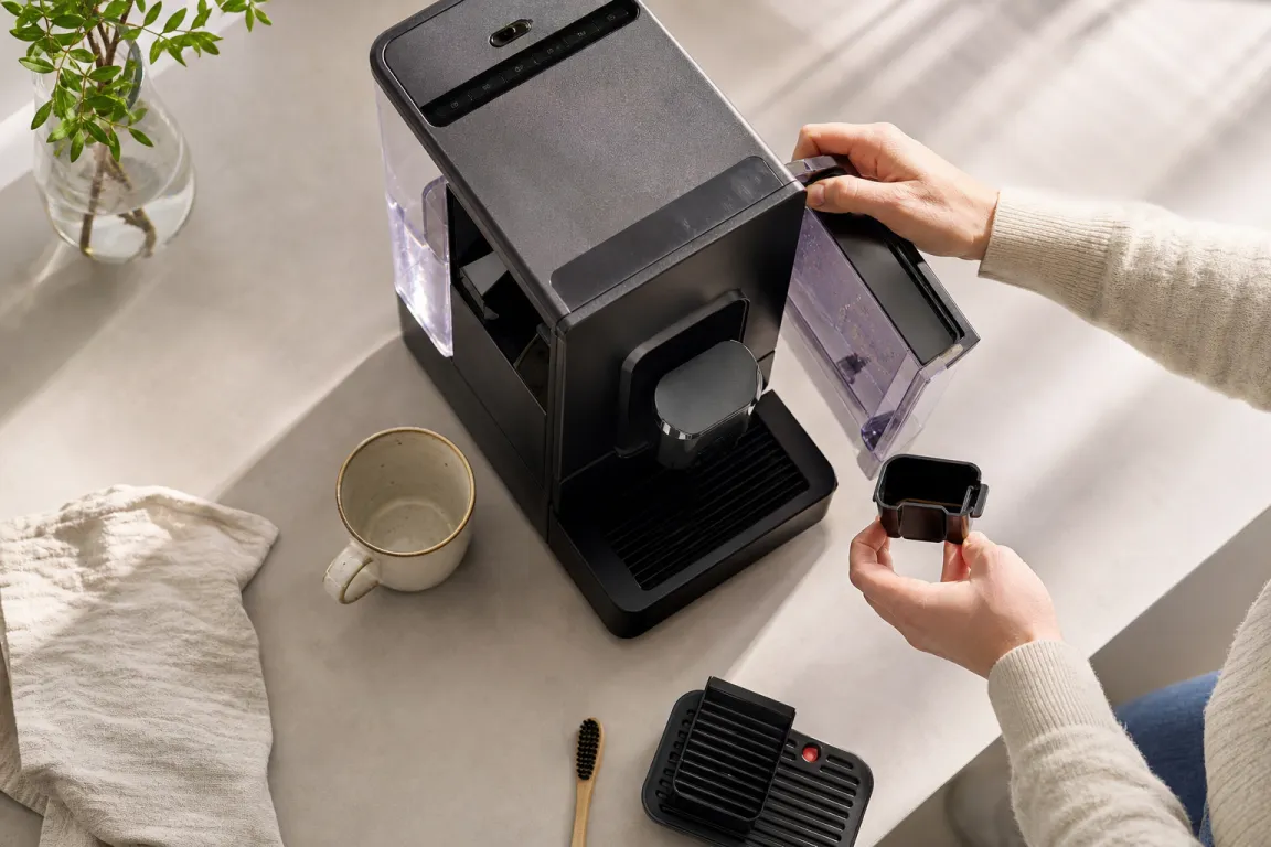 Person kontrollerar vattenbehållare och display på en kaffemaskin som visar felmeddelande